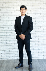 portrait of  young asian businessman in suit standing and smile with white brick background.