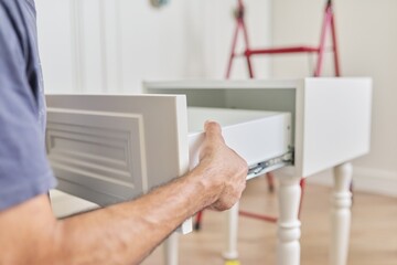 Assembly of wooden white bedside table at home, closeup of a worker's hand