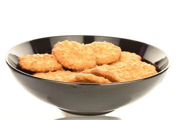 Several sweet torchetti cookies with oatmeal in a black ceramic plate, close-up, on a white background.
