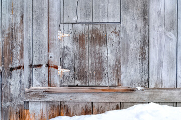 Close up of wooden building exterior with small square hinged window in winter