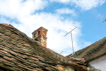 Fototapeta na wymiar Romanian ceramic shingle roof with brick chimney and old television antenna
