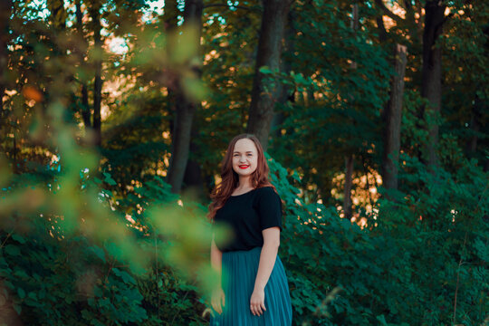 Girl in a turquoise skirt in a fairy forest. Smiling cute girl with red lipstick. Girl on the background of large tree branches