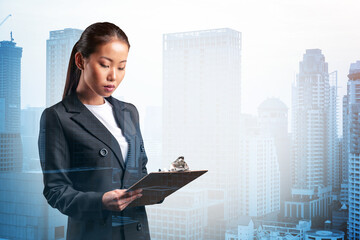 Attractive young Asian business woman in suit taking notes into the notebook, new career...