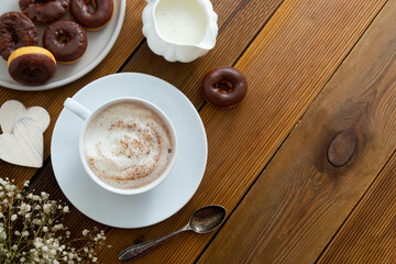 Cup of coffee,milk saucer and donuts, on wooden table with copy space.