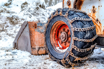 Old snow bulldozer with rusty blade and black tires wrapped with chains