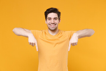 Young smiling unshaved caucasian man 20s in casual blank print design t-shirt point index two fingers down on workspace copy space area look camera isolated on yellow background studio portrait. © ViDi Studio