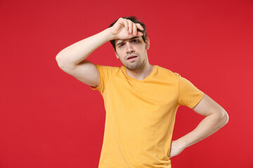 Fototapeta na wymiar Young tired sick ill stressed exhausted unshaved caucasian man 20s wearing casual basic yellow t-shirt put hand on forehead head having headache isolated on red color background studio portrait.
