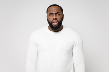 Concerned worried shocked dissatisfied young african american man 20s wearing casual basic sweater standing keeping mouth open looking camera isolated on white color wall background studio portrait.