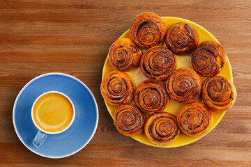 Homemade cinnamon rolls from yeast dough and cup of coffee espresso on wooden table. Top view.