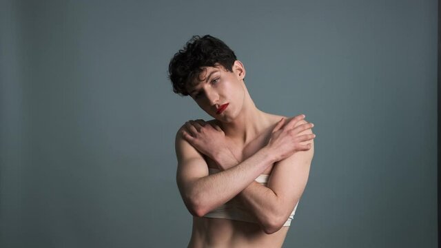 Androgyny. Transgender guy with makeup posing on grey background. Medium shot. Masculine and feminine characteristics in one person. Gender identity concept 4k
