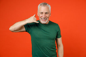 Smiling elderly gray-haired mustache bearded man wearing basic casual green t-shirt standing doing phone gesture like says call me back isolated on bright orange color background studio portrait.