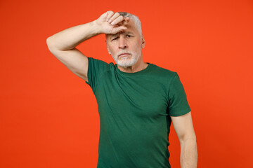 Fototapeta na wymiar Upset exhausted tired elderly gray-haired mustache bearded man wearing basic green t-shirt standing put hand on head looking camera isolated on bright orange color wall background studio portrait.