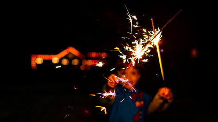 Naklejka na ściany i meble A blurred out boy waves sparklers at night celebrating New Year's Eve.