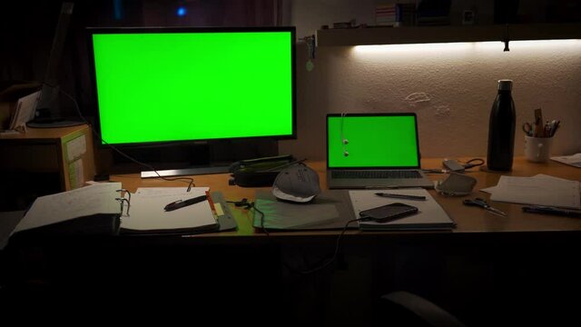 A messy desktop with a green-screen computer and display, a mask, stuff for study or school.