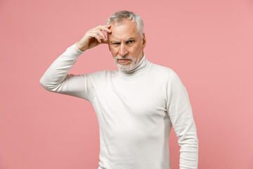 Preoccupied puzzled elderly gray-haired mustache bearded man wearing casual basic white turtleneck standing put hand on head looking aside isolated on pastel pink color background studio portrait.