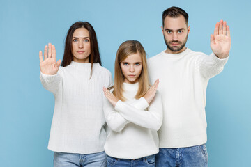 Displeased young parents mom dad with child kid daughter teen girl in sweaters showing stop gesture with palms crossed hands isolated on blue background studio portrait. Family day parenthood concept.