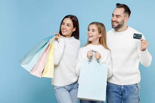 Cheerful Young Parents Mom Dad With Child Kid Daughter Teen Girl Hold Package Bags Purchases After Shopping Credit Bank Card Looking Aside Isolated On Blue Background. Family Day Parenthood Concept.