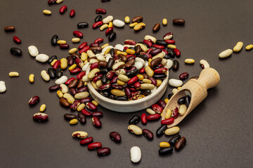 Mix of various dry legumes in ceramic bowl, scattered on black stone background
