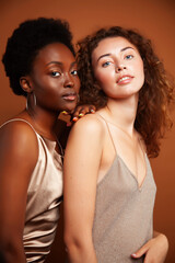 Obraz premium two pretty girls african and caucasian blond posing cheerful together on brown background, ethnicity diverse lifestyle people concept