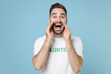 Excited cheerful young man in white volunteer t-shirt scream news with hands near mouth isolated on...