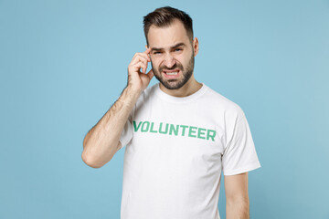 Worried tired young bearded man in white volunteer t-shirt put hand on head having headache...