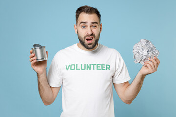 Perplexed worried young man in white volunteer t-shirt hold foil can looking camera isolated on...