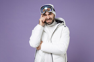 Worried sick skier man in white windbreaker jacket ski goggles mask put hand on head having headache spend weekend winter in mountains isolated on purple background. People lifestyle hobby concept.
