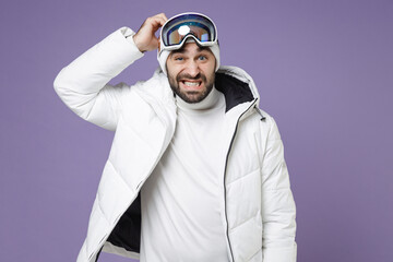 Preoccupied skier man in warm white windbreaker jacket ski goggles mask put hand on head spend extreme weekend winter season in mountains isolated on purple background. People lifestyle hobby concept.