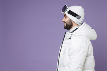 Side view of smiling skier man in warm white windbreaker jacket ski goggles mask spend extreme weekend winter season in mountains isolated on purple background studio. People lifestyle hobby concept. © ViDi Studio