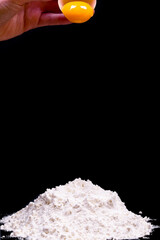 Egg held over the flour .Fresh raw egg in half shell on a black background
