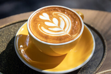 Cup of coffee with latte art on wooden table and morning sunlight with shadow through from window. Beautiful morning.