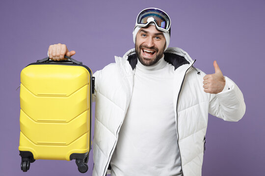 Cheerful Traveler Tourist Skier Man In White Jacket Ski Goggles Mask Hold Suitcase Showing Thumb Up Spend Weekend Winter In Mountains Isolated On Purple Background. People Lifestyle Hobby Concept.