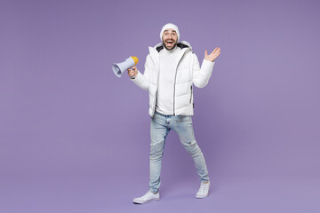 Full length surprised man in warm white padded windbreaker jacket hat screaming in megaphone spreading hands isolated on purple background studio portrait. People lifestyle cold winter season concept.