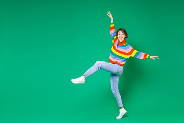 Full length side view of excited young brunette woman 20s in casual colorful sweater dancing...