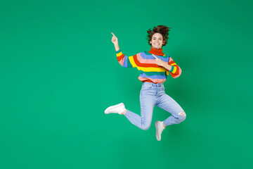 Fototapeta na wymiar Full length of smiling laughing pretty young brunette woman 20s in colorful sweater jumping point index fingers aside on mock up copy space isolated on bright green color background studio portrait.