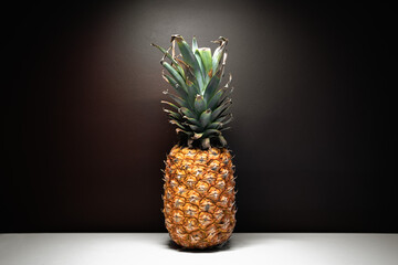 A close up portrait of an illuminated old shabby pineapple on a dark background. A pineapple diet concept.