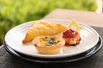 Spinach quiche, Pie and Cheesecake mini snack set on white plate in a garden.