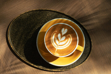 Cup of coffee with latte art on wooden table and morning sunlight with shadow through from window. Beautiful morning.