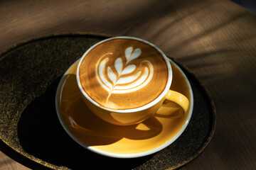 Cup of coffee with latte art on wooden table and morning sunlight with shadow through from window....