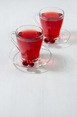 Healthy red herbal tea in transparent mug with ripe hawthorn berries in sunlight on white wood board, copy space, vertical.