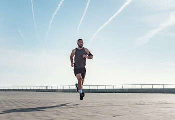 Fit young man running along seafront. Male runner jogging early in the morning. Fitness training outdoors. Workout during lockdown outside the gym.