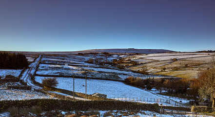 Snowy Nidderdale and late afternoon sun lights up moorland pastures, fields and a single track road. 