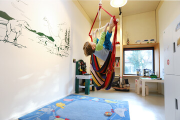 Ein vierjähriger Junge sitzt in einer Hängeschaukel in seinem Kinderzimmer