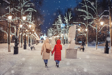 Happy female friends walk in the evening winter park on the sidewalk against the background of Christmas and New Year decorations in Ufa, Russia