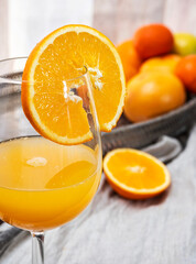 Crystal glass with orange juice, citrus background and cut orange. Colors yellow and orange.