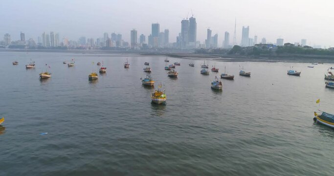 Flying over the fishermen's boats parked at the Koliwada next to Worli Fort, revealing the Mumbai Cityscape view of skyscrapers in the back with settlements to contrast.