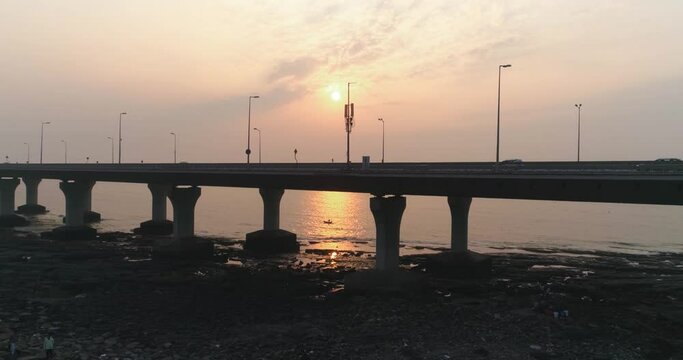 Fly by under the Bandra Worli Sea Link, revealing a fisherman in a boat with the sun setting in the back. Mumbai's iconic landmark looks even more cinematic in aerial view when captured with a drone.