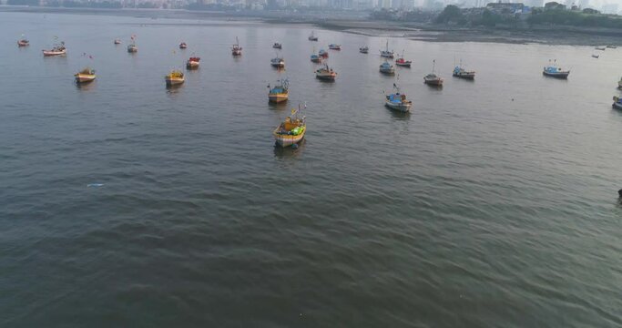 Flying over the fishermen's boats parked at the Koliwada next to Worli Fort, revealing the Mumbai Cityscape view of skyscrapers in the back with settlements to contrast.