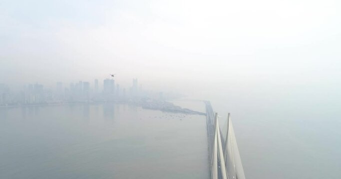 A drone shot at Bandra Worli Sea Link seen from an aerial view in slow motion. Cinematic drone movement with the iconic Mumbai Sea Link at the forefront and the city view in the background.