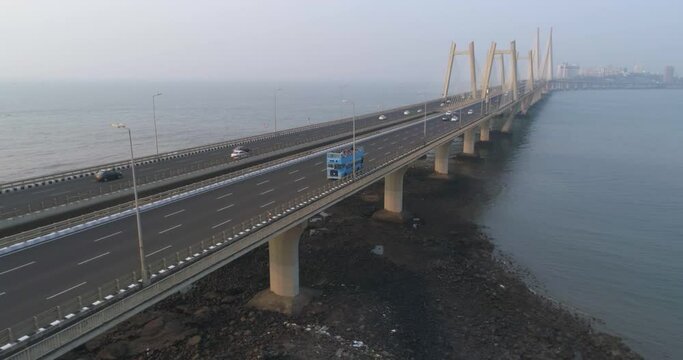 A drone shot at Bandra Worli Sea Link seen from an aerial view in slow motion. Cinematic drone movement with the iconic Mumbai Sea Link at the forefront and the city view in the background.